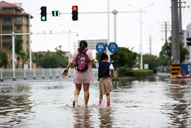 城市雨后严重积水的十字路口,远处可见交通信号灯、居民楼与行道树,路面被浑浊积水完全覆盖。